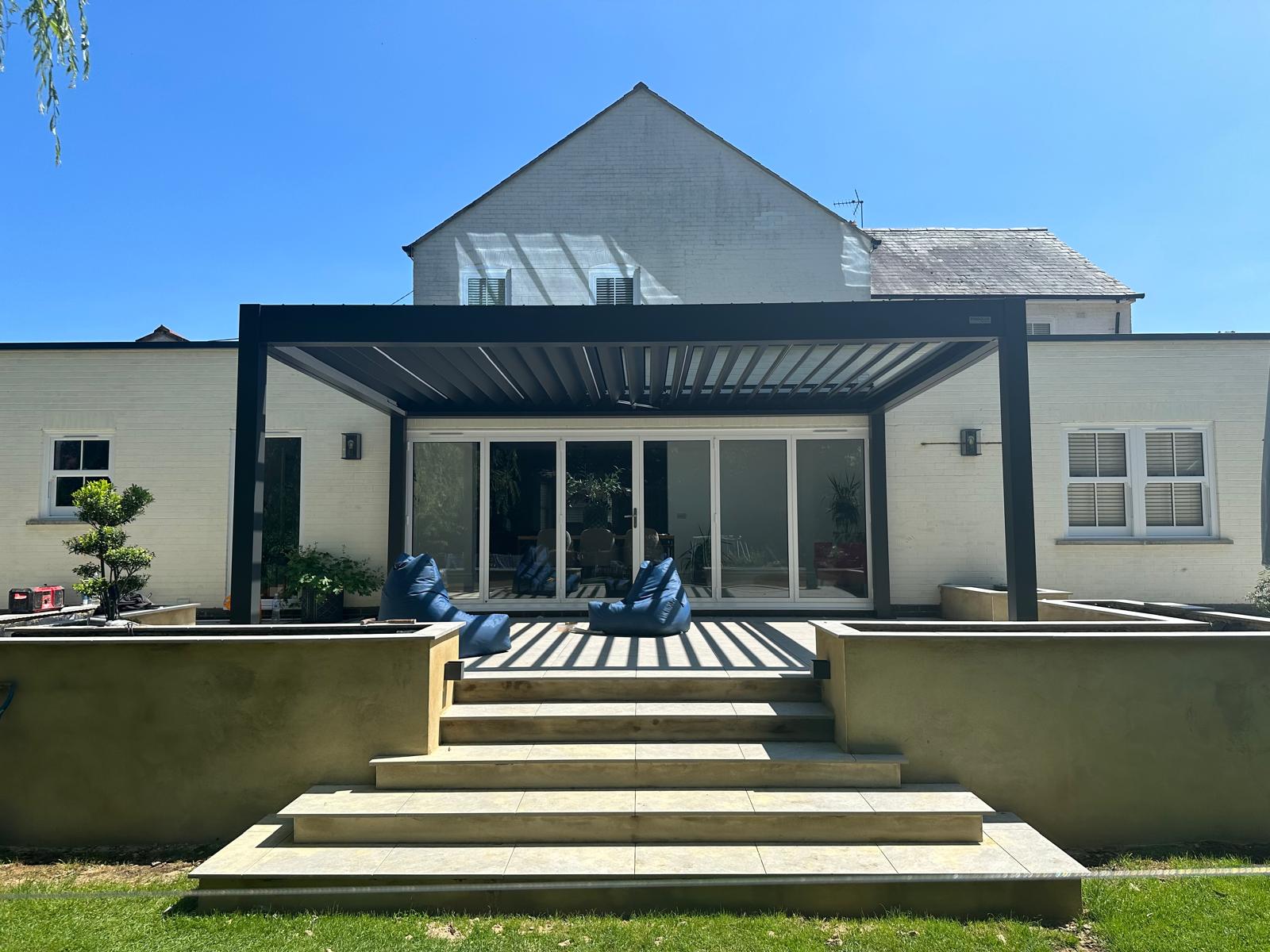 Aluminium louvred pergola over a porcelain terrace with rendered planters and steps by DBD Builders Ltd