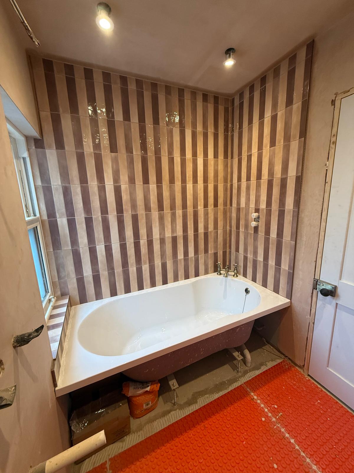 Bath installed against vertical patterned tiling with electric underfloor heating matting by DBD Builders Ltd