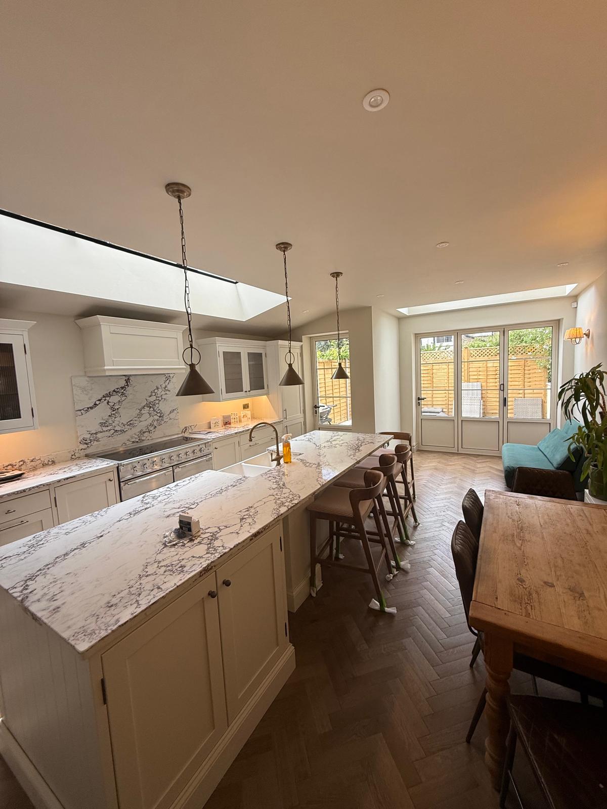 Finished shaker kitchen with marble island, pendant lights and herringbone flooring in a rear extension by DBD Builders Ltd