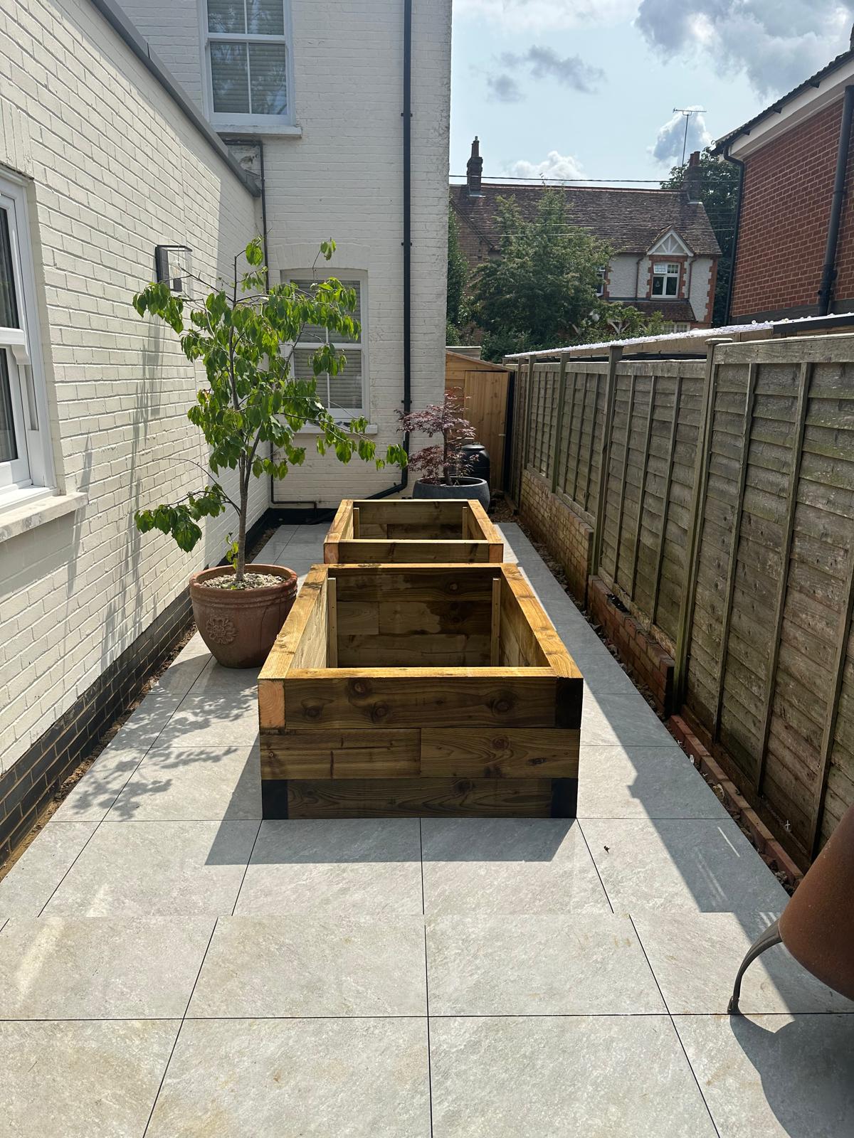 Large format porcelain paving with timber sleeper planters in a side garden by DBD Builders Ltd