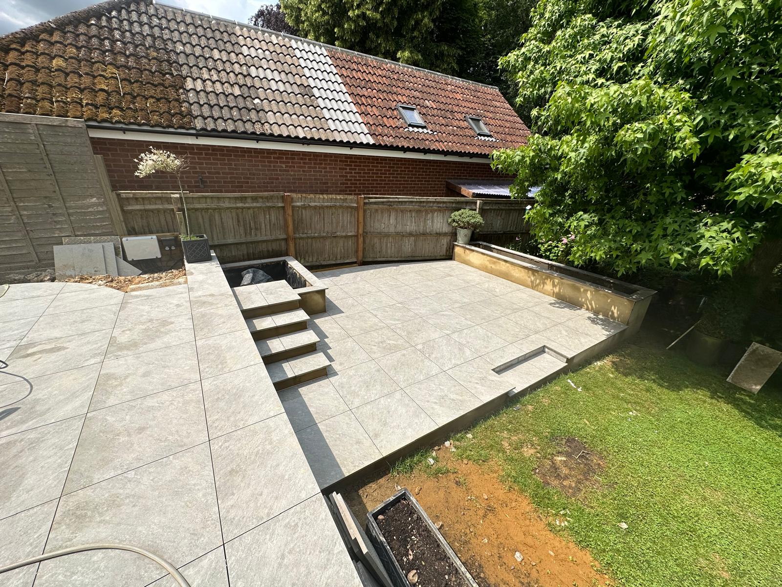 Grey porcelain patio with steel edged steps and a raised pond by DBD Builders Ltd
